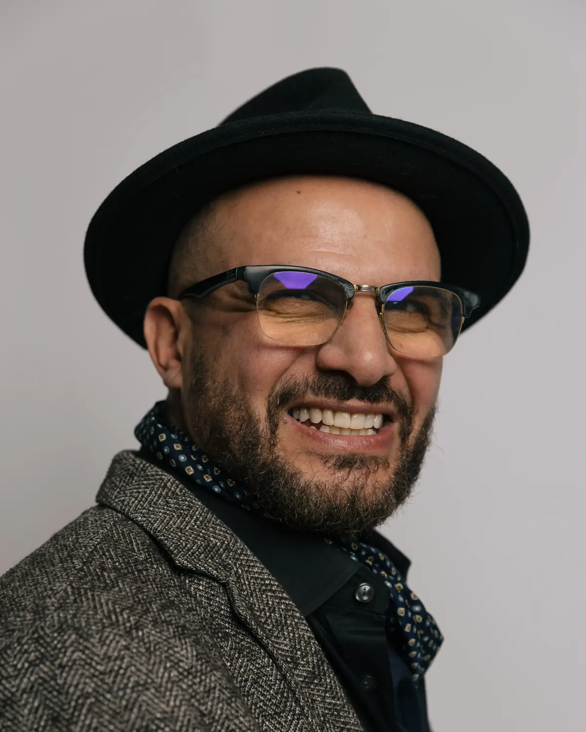 Eddine Belaid in Tweed mit Halstuch und Hut, lachend, Studioaufnahme 2025